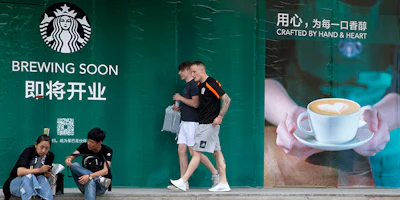 In this photo taken Wednesday, May 16, 2018, foreigners walk past a man and woman outside a Starbucks outlet under construction in Beijing, China. Starbucks and Chinese e-commerce giant Alibaba Group announced a coffee delivery venture on Thursday, Aug. 2, 2018, that adds to growing competition in China's booming delivery industry. (AP Photo/Ng Han Guan)