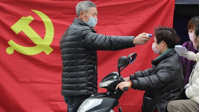 A volunteer stands in front of a Communist Party flag as he takes the temperature of a scooter driver at a roadside checkpoint in Hangzhou in eastern China's Zhejiang Province on Monday, Feb. 3.