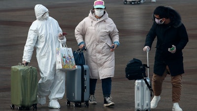 A passenger wearing a full-body protective suit catches the eyes of others as they walk out from the Beijing railway station in Beijing on Tuesday, Feb. 11. China's daily death toll from a new virus topped 100 for the first time and pushed the total past 1,000 dead, authorities said Tuesday after leader Xi Jinping visited a health center to rally public morale amid little sign the contagion is abating.