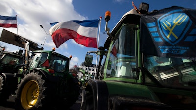 The Farmers Defense Force flag, right, and Dutch flags, fly in the wind on an intersection blocked by tractors in The Hague, Netherlands on Wednesday, Feb. 19. Dutch farmers, some driving tractors, poured into The Hague on Wednesday to protest government moves to rein in carbon and nitrogen emissions to better fight climate change.