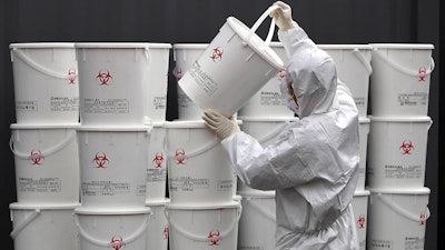 A worker in protective gear stacks plastic buckets containing medical waste from coronavirus patients at a medical center in Daegu, South Korea on Monday, Feb. 24. South Korea reported another large jump in new virus cases Monday a day after the the president called for 'unprecedented, powerful' steps to combat the outbreak that is increasingly confounding attempts to stop the spread.