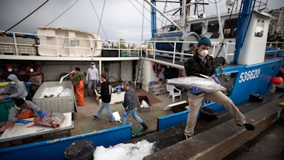 Fishing boat captain Nick Haworth, right, carries tuna to a dock for sale Friday, March 20, 2020, in San Diego. Haworth came home to California after weeks at sea to find a state all but shuttered due to coronavirus measures, and nowhere to sell their catch. A handful of tuna boats filled with tens of thousands of pounds of fish are now floating off San Diego's coast as they scramble to find customers.