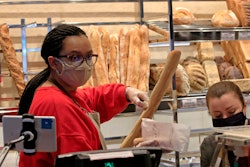 A vendor wearing a protective mask puts a baguette in a paper bag at a bakery in Paris on Monday, March 23.