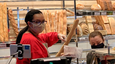A vendor wearing a protective mask puts a baguette in a paper bag at a bakery in Paris on Monday, March 23.