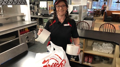 In this photo made on March 20, Frisch's Big Boy restaurant employee Nicole Cox bags up an order of toilet paper, among in-demand items including milk and bread the double-decker burger chain is now offering during the coronavirus outbreak in Cincinnati, OH.