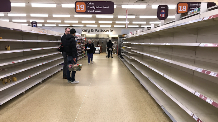 In this Thursday, March 19 file photo, people stand in an aisle of empty shelves in a supermarket in London, amid panic-buying due to the coronavirus outbreak.