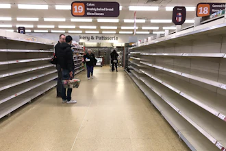 In this Thursday, March 19 file photo, people stand in an aisle of empty shelves in a supermarket in London, amid panic-buying due to the coronavirus outbreak.