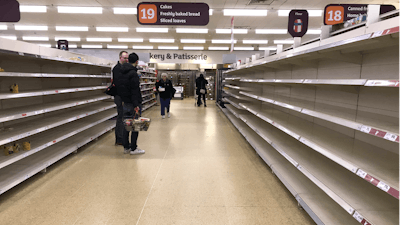 In this Thursday, March 19 file photo, people stand in an aisle of empty shelves in a supermarket in London, amid panic-buying due to the coronavirus outbreak.