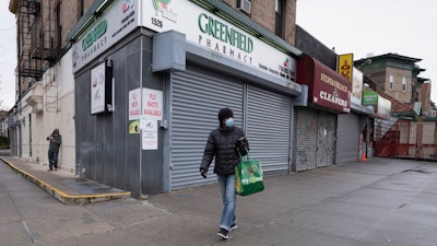 In this Friday, April 3, 2020, photo, a woman walks by local stores during the coronavirus pandemic in New York.