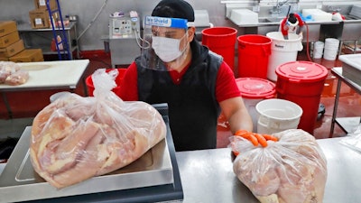 Amid concerns of the spread of COVID-19, Giovani Garcia weighs chicken at the butcher counter of El Rancho grocery store in Dallas, Monday, April 13, 2020.