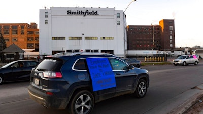 In this Thursday, April 9, 2020 photo, a car sporting a sign calling for a safe and healthy workplace drives past Smithfield Foods, Inc. in Sioux Falls. during a protest on behalf of employees after many workers complained of unsafe working conditions due to the COVID-19 outbreak.