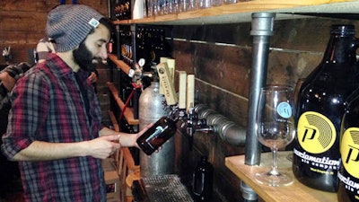 In this Friday, April 8, 2016 photo, Tom Pereira, tasting room manager at Proclamation Ale Co., fills a 32-ounce bottle of beer for a customer to take home during the release of a new beer in West Kingston, R.I. The ale house is urging lawmakers to remove the limit on the amount breweries can sell to visitors on site for consumption off premises.