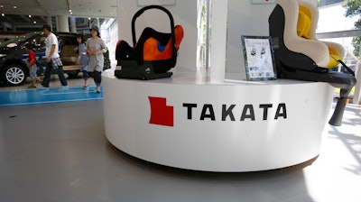 In this Wednesday, May 4, 2016 photo, a family walk by child seats manufactured by Japanese auto parts maker Takata Corp. at an automaker's showroom in Tokyo. Takata, which also makes seat belts, is expecting a loss instead of a profit for the fiscal year that ended in March because of ballooning costs from a massive global air-bag recall. Takata is projecting an annual net loss of $120 million.