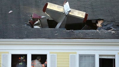 Firefighters investigate the scene after a single-engine aircraft crashed into a building across the Merrimack River from Lawrence Municipal Airport, Tuesday, Feb. 28, 2017, in Methuen, Mass. According to police, the pilot of the home-built plane was killed, while no one in the building was hurt.