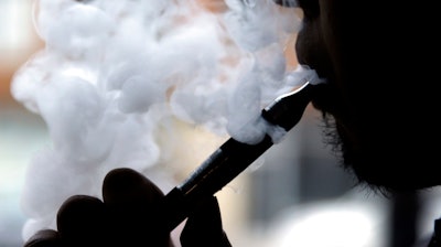 In this April 23, 2014 file photo, a man smokes an electronic cigarette in Chicago. A House panel is again trying to exempt increasingly popular e-cigarettes from new Food and Drug Administration rules. The legislation approved July 12, 2017, by the Republican-controlled Appropriations Committee would prevent the FDA from requiring retroactive safety reviews of e-cigarettes already on the market. It would exempt some premium and large cigars from those same regulations. E-cigarette products introduced in the future would face the safety reviews.