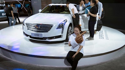 A woman poses for a photo in front of a CT6 Cadillac during the Consumer Electronics Show Asia 2018 in Shanghai, China on Friday, June 15, 2018. President Donald Trump is poised to hike the price of Chinese-made flat-screen TVs and ultrasound machines for American buyers. They are part of a tech imports worth up to $50 billion on which Trump is preparing to slap 25 percent tariffs in response to complaints Beijing steals or pressures foreign companies to hand over technology.
