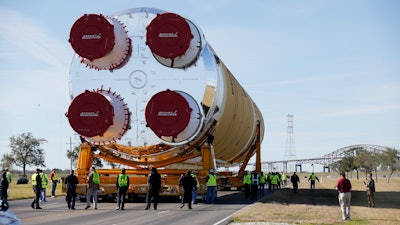 Security personnel walk with the core stage of NASA's Space Launch System rocket, that will be used for the Artemis 1 Mission, as it is moved to the Pegasus barge, at the NASA Michoud Assembly Facility where it was built, in New Orleans, Wednesday, Jan. 8, 2020. It will be transported to NASA's Stennis Space Center in Mississippi for its green run test.