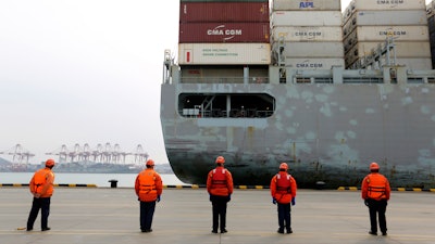 In this Tuesday, Feb. 4, 2020, photo, workers watch a container ship arrive at a port in Qingdao in east China's Shandong province.