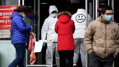 A worker in overalls screen for fever at the entrance to a supermarket in Beijing Thursday, Feb. 27, 2020.