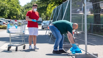 Employees of a grocery store deliver ordered products in plastic bags to residents of apartment buildings that are partly under quarntine due to a new coronavirus outbreak in Verl, Germany on Wednesday, June 24.