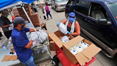 Wearing masks amid concerns of the spread of COVID-19, volunteers Karen Cooperstein, right, and Edwin Chinchilla, left, prepare food for the pubic during a drive through food pantry distribution by Catholic Charities in Dallas, Thursday, July 2, 2020.