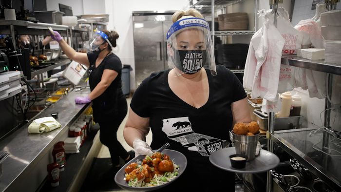In this July 1, 2020, file photo, a waitress takes a food order from the kitchen at Slater's 50/50 in Santa Clarita, CA.