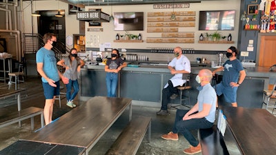 In a July 2020 photo provided by Wolf's Ridge Brewing, owner Bob Szuter, employees Allison Randolph and Alicia Herrmann, sous chef Andy Zamagias, general manager Corey Schlosser and employee Andy Powell, from left, gather inside the restaurant's tap room in Columbus, Ohio. Szuter says he’s trying to figure out new ways to bring in revenue, focusing more on the brewery side of the business until it’s safe to have a full dining room.
