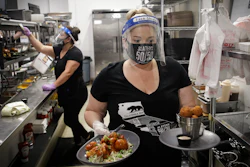 In this July 1, 2020, file photo, a waitress takes a food order from the kitchen at Slater's 50/50 in Santa Clarita, CA.