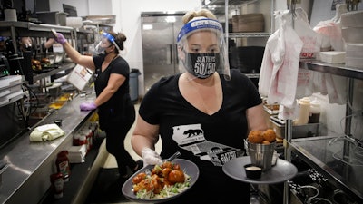 In this July 1, 2020, file photo, a waitress takes a food order from the kitchen at Slater's 50/50 in Santa Clarita, CA.