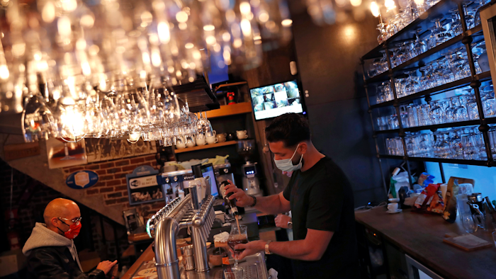 A bartender, wearing a face mask to fight against the spread of coronavirus, serves a beer to a customer in a pub in Brussels on Wednesday, Oct. 7.