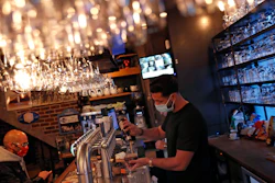 A bartender, wearing a face mask to fight against the spread of coronavirus, serves a beer to a customer in a pub in Brussels on Wednesday, Oct. 7.