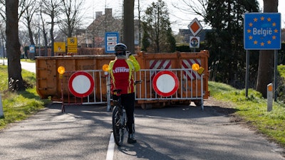 In this March 23, 2020 photo, a cyclist takes images of a barricaded backroad used by locals on the Netherlands border with Belgium between Chaam, southern Netherlands, and Meerle, Northern Belgium.