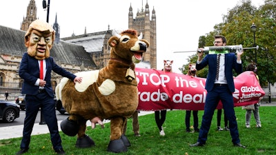A man imitates the injection of hormones into a man in a cow costume in Parliament Square, as part of a day of action against the US trade deal, in London on Saturday, Oct. 24.