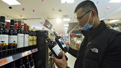 A man wearing a face mask compares two bottles of Australian wine at a supermarket in Hangzhou in east China's Zhejiang province on Nov. 27.