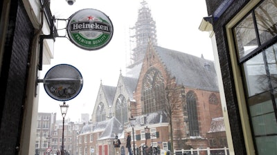 A Heineken sign sits on the facade of a bar, closed because of the coronavirus lockdown in Amsterdam, Sunday, Feb. 7, 2021. Dutch beer brewer Heineken said Wednesday it plans to cut 8,000 staff, nearly 10% of its global workforce, as part of a cost-cutting reorganization after a pandemic-dominated year that saw it sink to a net loss of 204 million euros ($248 million).