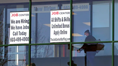 A woman, wearing a protective mask due to the COVID-19 virus outbreak, walks past the signs of an employment agency on March 2 in Manchester, NH.