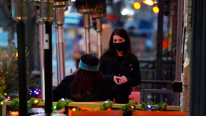 In this Dec. 28, 2020, file photo, a server wears a face mask while tending to a patron sitting in the outdoor patio of a sushi restaurant, in downtown Denver.