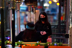 In this Dec. 28, 2020, file photo, a server wears a face mask while tending to a patron sitting in the outdoor patio of a sushi restaurant, in downtown Denver.