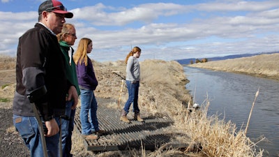 In this March 2, 2020, file photo, farmer Ben DuVal with his wife, Erika, and their daughters, Hannah, third from left, and Helena, fourth from left, stand near a canal for collecting run-off water near their property in Tulelake, Calif.