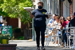 A member of the wait staff delivers food to outdoor diners along the sidewalk at the Mediterranean Deli restaurant in Chapel Hill, NC on April 16.
