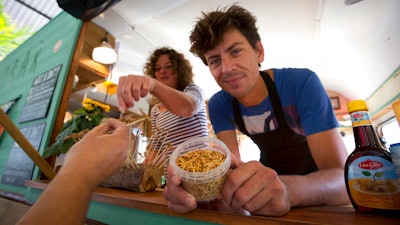 In this In this Sept. 21, 2014 file photo, Microbar food truck owner Bart Smit holds a container of yellow mealworms during a food truck festival in Antwerp, Belgium.