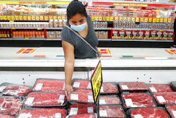 In this April 29, 2020 photo, a shopper wears a mask as she looks over meat products at a grocery store in Dallas.