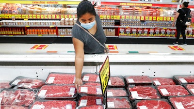 In this April 29, 2020 photo, a shopper wears a mask as she looks over meat products at a grocery store in Dallas.