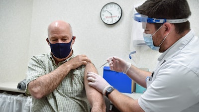 In this April 1, 2021 file photo, Montana Gov. Greg Gianforte receives a shot of the Pfizer COVID-19 vaccine from pharmacist Drew Garton at a Walgreen's pharmacy in Helena, Mont. While large companies across the U.S. have announced that the COVID-19 vaccine will be required for their employees to return to work in-person, there is one state where such requirements are banned: Montana.