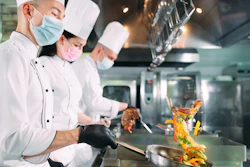 Chefs In Protective Masks And Gloves Prepare Food In The Kitchen Of A Restaurant Or Hotel 1269125983 2125x1416 (1)