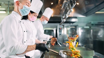 Chefs In Protective Masks And Gloves Prepare Food In The Kitchen Of A Restaurant Or Hotel 1269125983 2125x1416 (1)