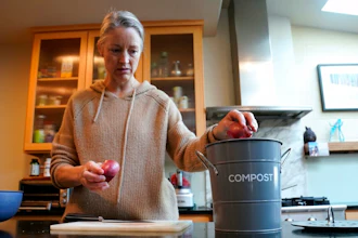 Joy Klineberg tosses an onion peel into container to be used for composting while preparing a family meal at her home in Davis, Calif., Tuesday, Nov. 30, 2021. In January 2022, new rules take effect in California requiring people to recycle their food waste to be combusted or turned into energy. Davis already requires residents to recycle their food waste into the yard waste bin instead of the trash.