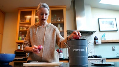 Joy Klineberg tosses an onion peel into container to be used for composting while preparing a family meal at her home in Davis, Calif., Tuesday, Nov. 30, 2021. In January 2022, new rules take effect in California requiring people to recycle their food waste to be combusted or turned into energy. Davis already requires residents to recycle their food waste into the yard waste bin instead of the trash.