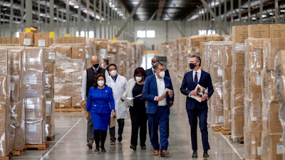 Gov. Gavin Newsom, right, walks through rows of boxed Personal protective equipment, PPE, with dignitaries and elected officials, as he prepares to announce the next phase of California's COVID-19 response called 'SMARTER,' during a press conference at the UPS Healthcare warehouse in Fontana, CA on Feb. 17, 2022.