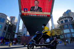A delivery courier rides past a large video screen at a shopping mall showing Chinese Premier Li Keqiang speaking during the opening session of the annual meeting of China's National People's Congress (NPC) in Beijing, Saturday, March 5, 2022.